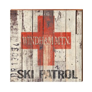 Könnte beinhalten: Quadratisches Holzschild mit einem rustikalen, verwitterten Design. Das Schild zeigt ein großes rotes Kreuz mit den Worten "WINDHAM MTN." und "SKI PATROL" in schwarzer Schrift. Der Hintergrund besteht aus verwitterten Holzplanken.