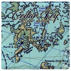 Könnte beinhalten: Ein quadratischer Untersetzer mit einer Seekarte von Cedar Key, Florida. Die Karte zeigt Landmassen in Beige, Wasser in Hellblau und Navigationslinien in Dunkelblau. Der Text umfasst Cedar Key, 29.13 N 83.03 W sowie verschiedene Orientierungspunkte.