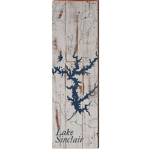 May include: Wooden wall art featuring a map of Lake Sinclair in navy blue against a distressed white background. The wood has visible grain and cracks, with the lake's outline prominently displayed. The words "Lake Sinclair" are printed at the bottom.