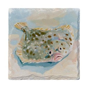 May include: A square stone coaster featuring a painted illustration of a flatfish with a mottled green and brown body, dark spots, and light-colored fins. The fish is depicted against a soft, pale blue and sandy beige background.