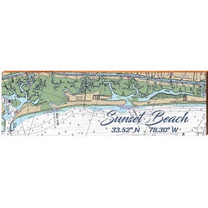 May include: A wooden wall art piece featuring a nautical chart of Sunset Beach, North Carolina. The map shows the coastline, waterways, and depth contours in shades of blue, green, and beige. The words "Sunset Beach" are written in a cursive font.