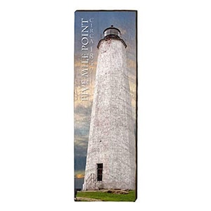 Könnte beinhalten: Rechteckiges Holzschild mit einem weißen Leuchtturm vor bewölktem Himmel. Der Text "FIVE MILE POINT CIRCA 1847" ist vertikal auf der linken Seite aufgedruckt. Der Leuchtturm hat eine schwarze Spitze und eine kleine Tür.