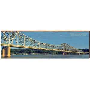 May include: A panoramic image of the Shell Knob Bridge over Table Rock Lake. The bridge is a steel truss design, painted in a light green color, and spans across the water. The sky is a clear blue, and the image is framed in a wooden border.