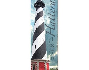 May include: A vertical wooden sign featuring a lighthouse with black and white spiral stripes. The base is red with white trim. The word "Hatteras" and the year "1870" are printed on the sign.
