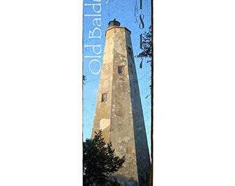 May include: A vertical wooden sign featuring a weathered image of the Old Baldy lighthouse. The lighthouse is beige with a dark top, set against a blue sky. Text includes "Old Baldy" and "Circa 1817".