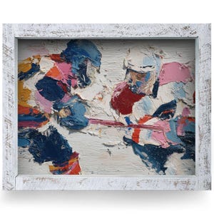 May include: Abstract oil painting of two hockey players in action, framed in a distressed white wooden frame. The artwork features thick brushstrokes in shades of blue, pink, red, and white, creating a textured and dynamic scene.