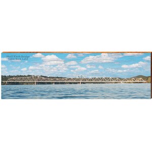 May include: A panoramic image of the Shell Knob Bridge over Table Rock Lake. The white bridge spans the blue water. The sky is blue with white clouds. The text "Shell Knob Bridge Table Rock Lake" is in the upper left corner.