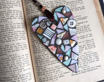 May include: Heart-shaped mosaic bookmark with a dark brown ribbon. The mosaic is made of various colorful tiles, buttons, and beads, resting on the pages of an old book. A unique, handmade gift.