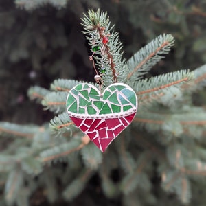 May include: A mosaic heart ornament with green and red glass pieces, hanging from a pine branch. The heart is divided into two sections, with a silver border. The ornament is decorated with small red and green beads.