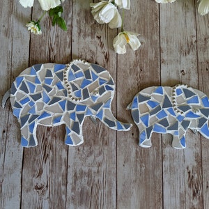 K&ouml;nnte beinhalten: Zwei Mosaik-Elefantenfiguren in Blau-, Grau- und Wei&szlig;t&ouml;nen. Die Elefanten haben Perlenakzente und sind auf einer Holzoberfl&auml;che angeordnet. Der gr&ouml;&szlig;ere Elefant ist etwa 25 cm lang.
