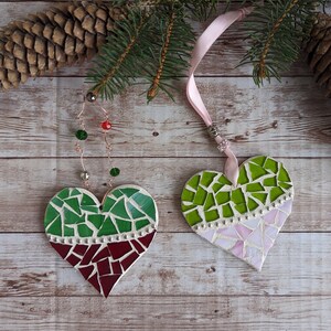 May include: Two heart-shaped mosaic ornaments. One features green and burgundy tiles, the other green and pink. Both have a white border and are suspended by ribbons. Festive holiday decor.