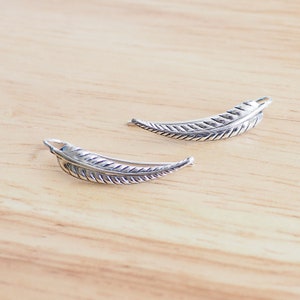 May include: A pair of silver feather earrings. The earrings are shaped like a feather and have a textured surface.