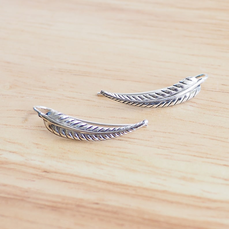 May include: A pair of silver feather earrings. The earrings are shaped like a feather and have a textured surface.