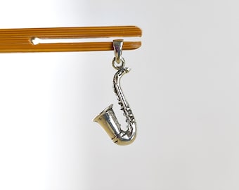May include: A silver saxophone charm pendant. The charm is detailed and has a realistic design.