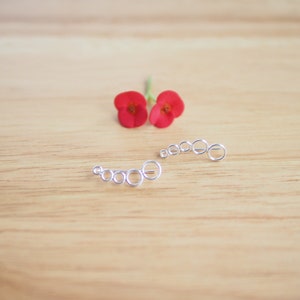 May include: A pair of silver ear cuffs with a graduated circle design. The cuffs are on a wooden surface.