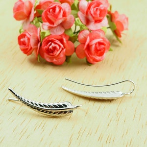 May include: A pair of silver earrings shaped like a leaf. The earrings are delicate and have a textured surface.