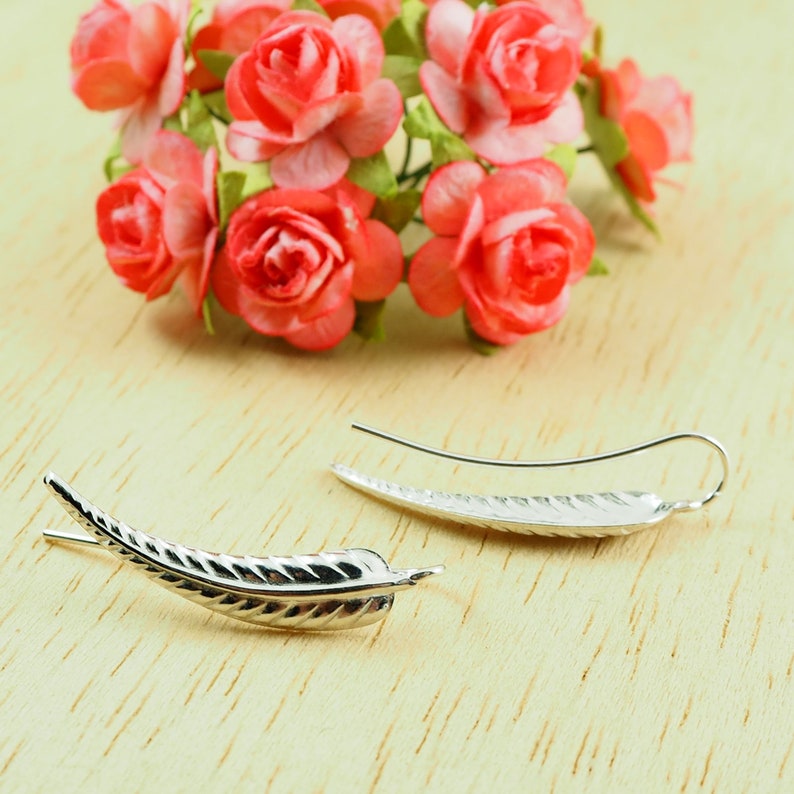 May include: A pair of silver earrings shaped like a leaf. The earrings are delicate and have a textured surface.