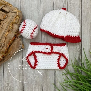 May include: A white crocheted baseball hat with a red brim, a white crocheted diaper cover with a red trim, and a white crocheted baseball with red stitching.