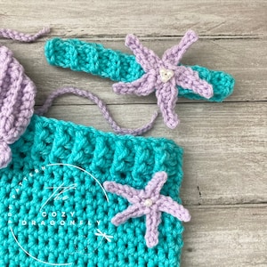 May include: A teal crochet mermaid tail with two purple crocheted starfish with pearl accents. The text "PDF PATTERN by COZY DRAGONFLY" is visible on the tail.