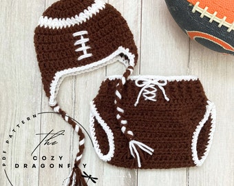 May include: A crocheted football hat and diaper set for a baby. The hat is brown with white stitching and a white pom-pom. The diaper is brown with white stitching and a white lace tie.