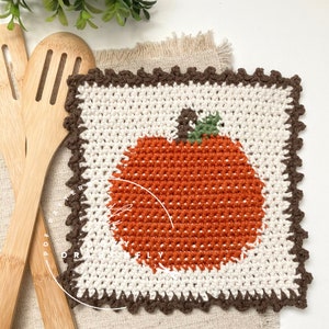 May include: A crocheted pumpkin pot holder with a brown border. The pumpkin is orange with a green stem and leaves.