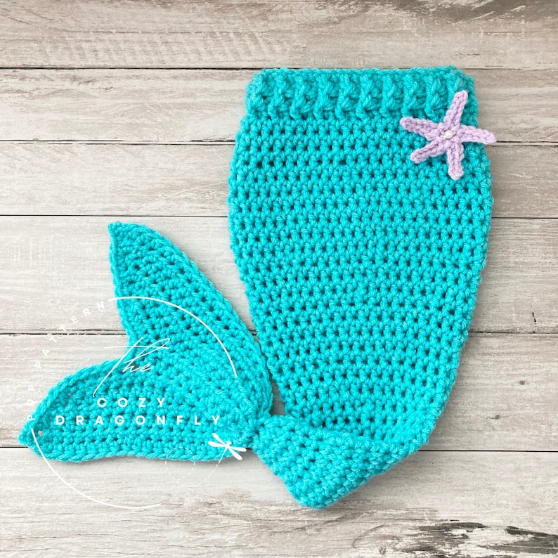 May include: A turquoise crocheted mermaid tail with a purple starfish on the top. The tail is made of yarn and is a handmade item.