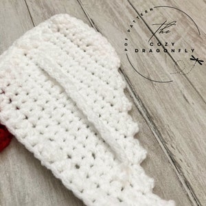 May include: White crocheted fabric with a scalloped edge. The fabric is folded in half, creating a seam down the center. The fabric is on a wooden surface.