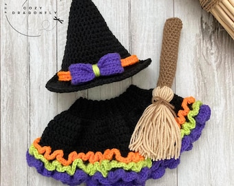 May include: Crocheted Halloween witch costume set, including a black pointed hat with purple bow and orange trim, a black skirt with purple, green, and orange trim, and a brown broom. The Cozy Dragonfly pattern is visible.