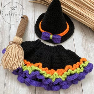 May include: A crochet Halloween costume set featuring a black witch hat with orange trim and a purple bow, a black skirt with orange, green, and purple trim, and a brown and tan broom. The Cozy Dragonfly PDF Pattern logo is in the upper left corner.