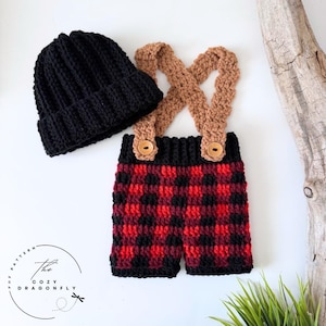 May include: A black crocheted beanie and matching crocheted overalls with tan straps, wooden buttons, and a red and black buffalo plaid pattern. The image includes the text The Cozy Dragonfly Pattern in a circular logo design.