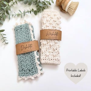 Pode incluir: Dois panos de prato feitos à mão em crochê, um em verde-água com acabamento branco e o outro em creme. Cada um é embrulhado com uma etiqueta de papel castanho que diz "Handmade Dishcloth" e "Handmade Washecloth".