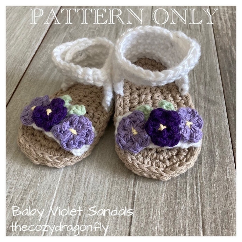 K&ouml;nnte beinhalten: H&auml;kelmuster f&uuml;r Babysandalen mit einem violetten Blumendesign. Die Sandalen sind beige mit wei&szlig;en Riemen und violetten und gr&uuml;nen Blumen.