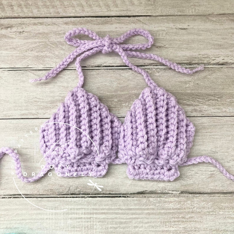 May include: A lavender crocheted seashell top with adjustable straps. The top is made of a soft, textured yarn and has a delicate, feminine design.