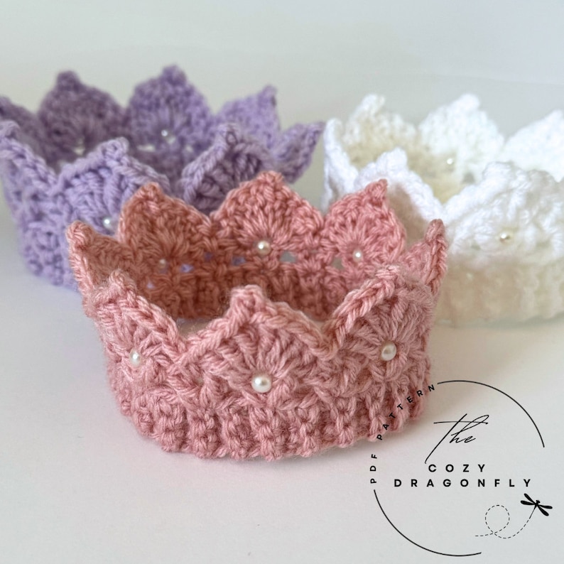 May include: Three crocheted crowns in pink, purple, and white with pearl embellishments. The crowns are handmade and have a delicate, feminine design.