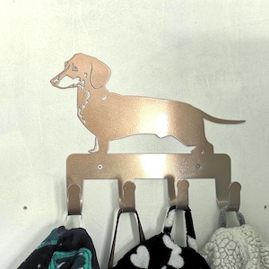 May include: A copper-coloured metal dachshund silhouette wall hook with five hooks. The dachshund is standing on a metal base. The hooks are empty.