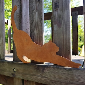 May include: A rusty metal silhouette of a cat stretching, mounted on a wooden fence.