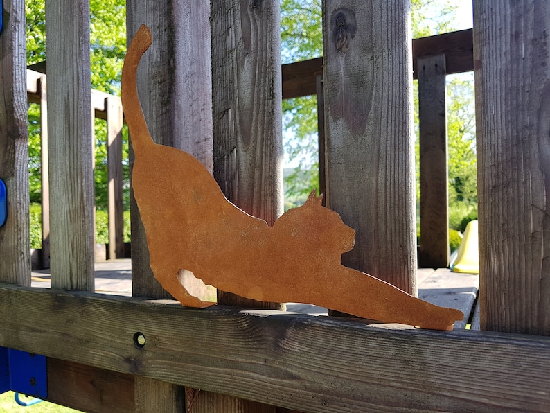 May include: A rusty metal silhouette of a cat stretching, mounted on a wooden fence.