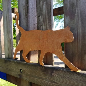 May include: A rusty metal cat silhouette, mounted on a wooden fence post. The cat is facing right and has a long tail.