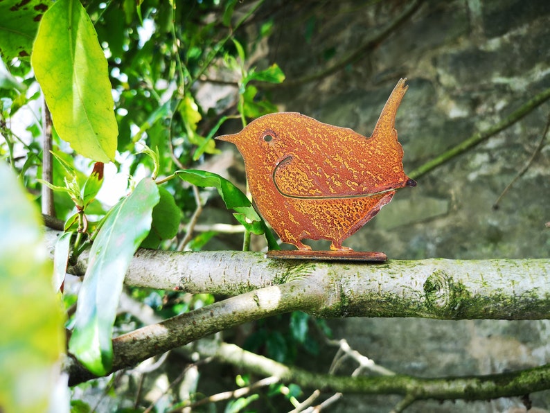 May include: A rusty orange metal bird sculpture perched on a branch. The bird has a rounded body and a long tail.