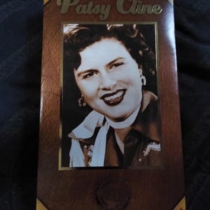 Puede incluir: Caja marrón con un retrato en blanco y negro de Patsy Cline. La caja tiene letras doradas que dicen "Patsy Cline". La caja tiene una textura similar al cuero con esquinas doradas.