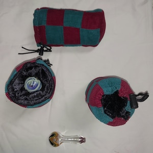 May include: An assortment of items including a glass pipe, three corduroy pouches, and a marble. The pouches are teal and burgundy, with one in a checkerboard pattern. The marble is white, blue, and purple. The glass pipe has yellow, orange, and black accents.
