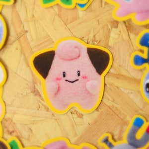 May include: A pink and brown cartoon character with a yellow outline. The character has a round body with a small head and a big smile. The character is on a light brown background.