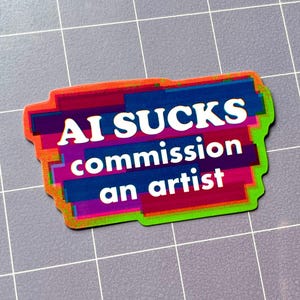 May include: A vibrant sticker with the message "AI SUCKS commission an artist." The design features layers of orange, red, blue, and green. The text is in white.