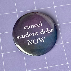 May include: A round button with a purple, blue, and black gradient background. The text "cancel student debt NOW" is printed in white on the button.
