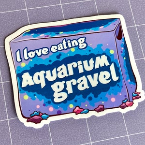 May include: A purple and blue box with the text "I love eating Aquarium Gravel" on it. The box is surrounded by small, colorful rocks.