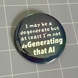 May include: A circular pin-back button with a dark, iridescent, galaxy-like background. The text printed in white reads: I may be a degenerate but at least I'm not deGenerating that AI. The button has a glossy finish and a smooth, rounded edge.