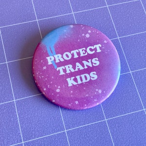 May include: A pink and blue button with white text that reads "PROTECT TRANS KIDS".