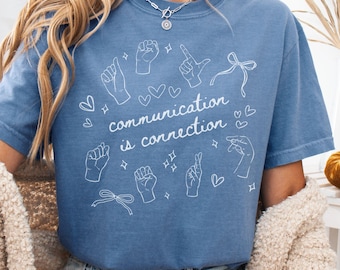 May include: Blue jean t-shirt with white line art of hand gestures and the phrase "communication is connection." The shirt features a crew neck and short sleeves. The design includes hearts, bows, and stars.