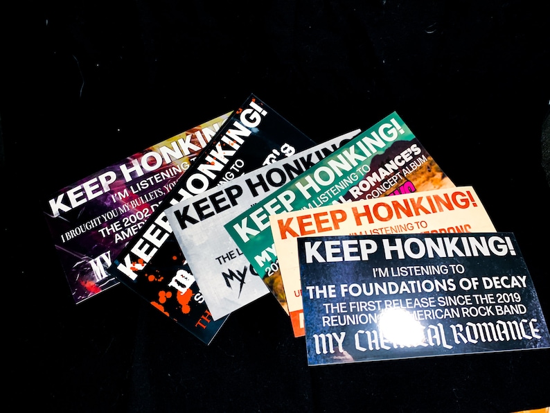 May include: A collection of rectangular stickers with the text "KEEP HONKING!" in bold, white letters. The stickers feature additional text, including "I'm listening to" and band names. The color schemes vary, with backgrounds in black, white, and orange.