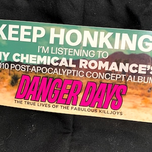 May include: Rectangular sticker with the text "KEEP HONKING! I'M LISTENING TO MY CHEMICAL ROMANCE'S 2010 POST-APOCALYPTIC CONCEPT ALBUM DANGER DAYS THE TRUE LIVES OF THE FABULOUS KILLJOYS" in white and pink lettering against a teal and desert landscape background.